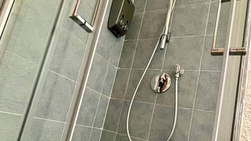 A shower area with a glass door, a handheld showerhead, and a wall-mounted control panel.