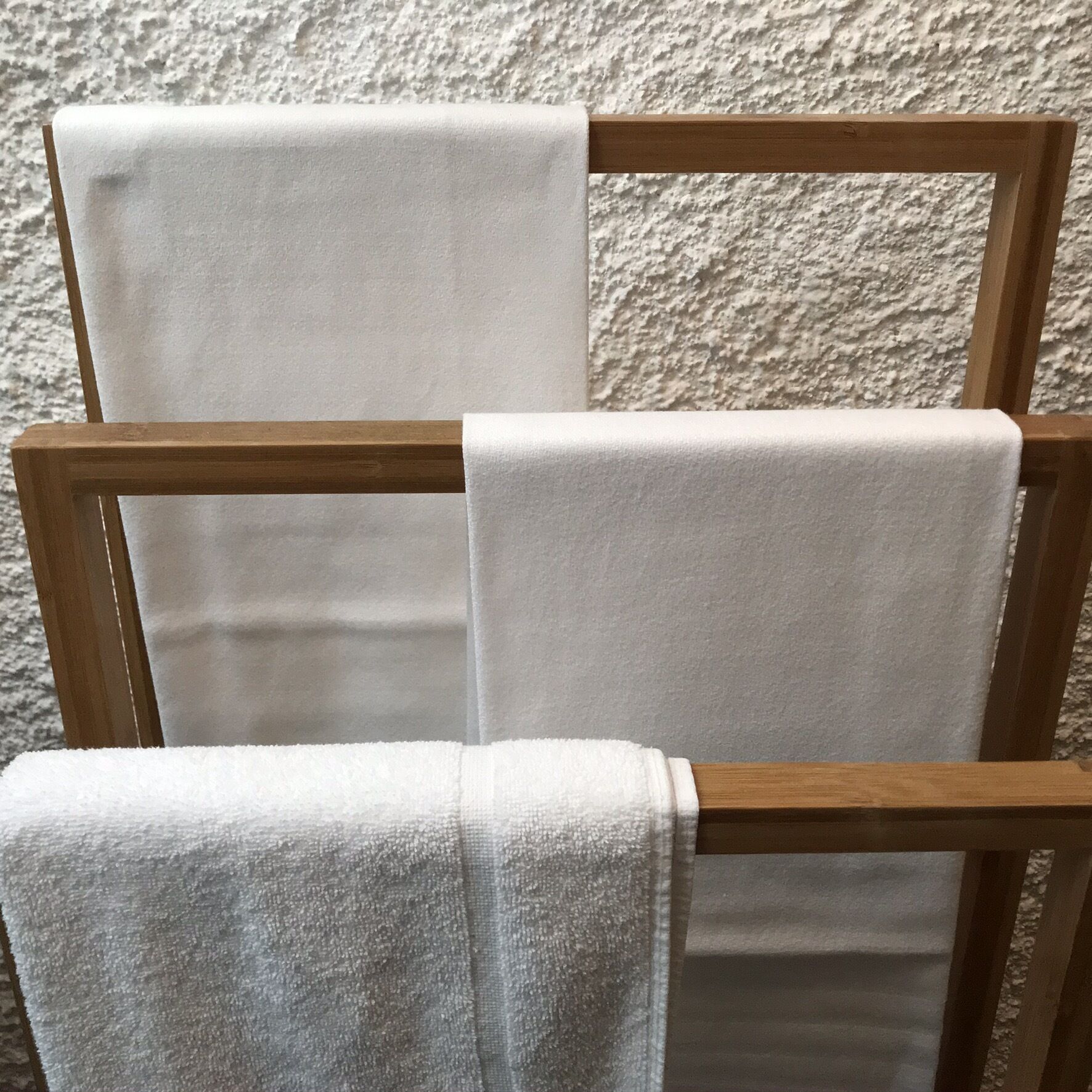 Ein hölzerner Handtuchhalter mit drei weißen Handtüchern.