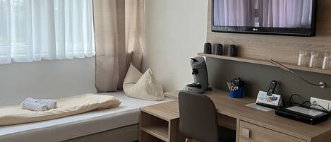 Habitación de hotel con cama, escritorio, silla, televisión y ventana con cortinas.