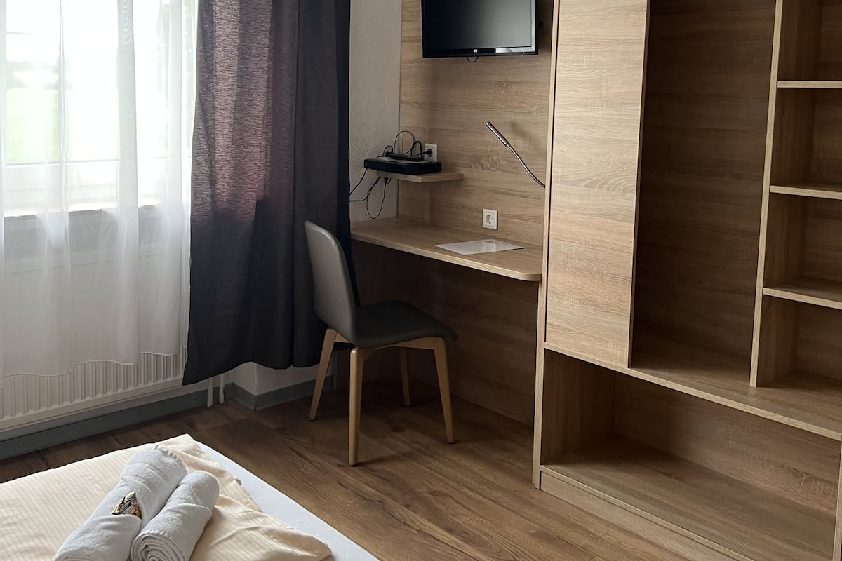 Una habitación de hotel con un escritorio de madera, un televisor, una silla y un armario.
