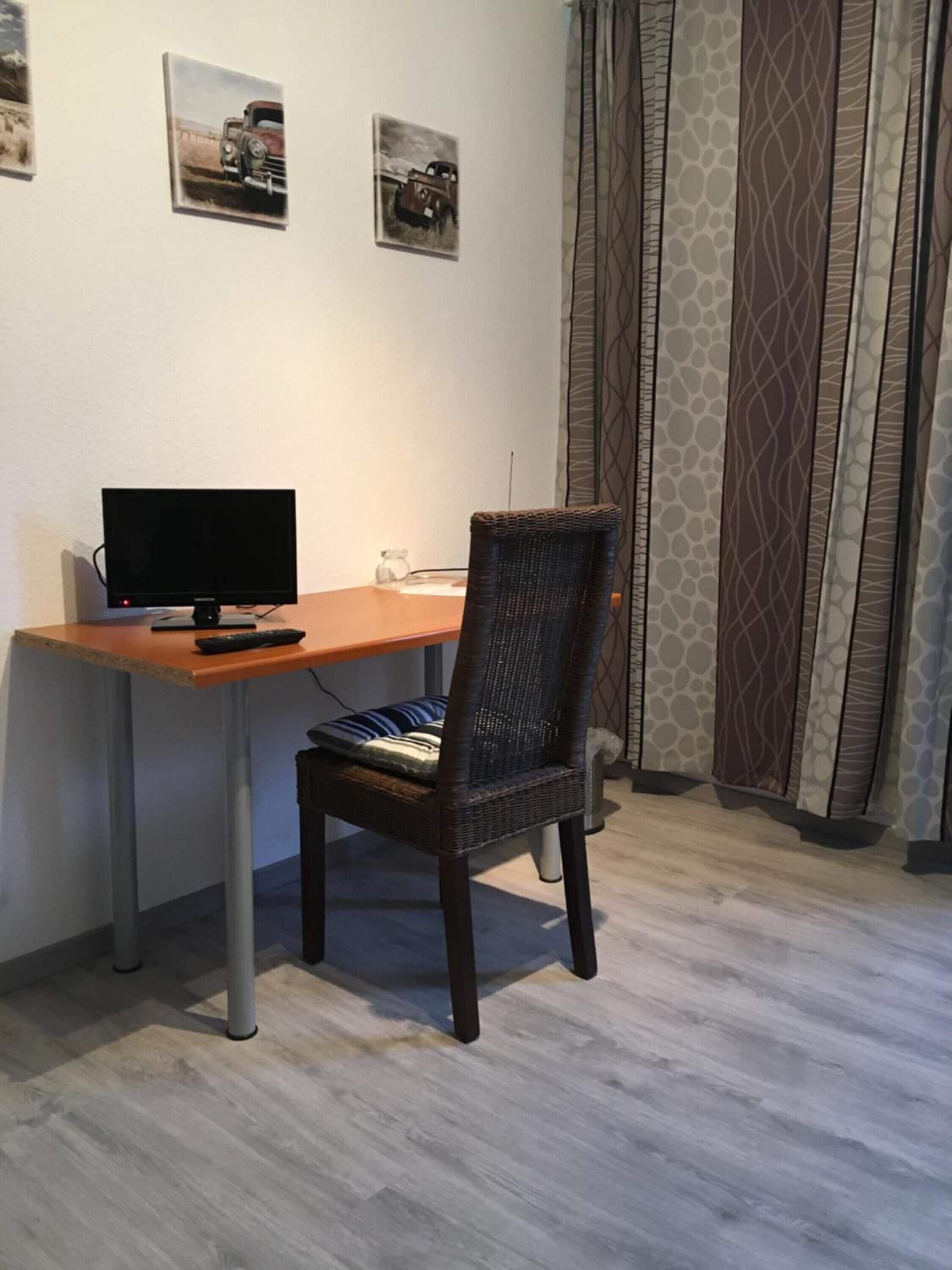 A room with a desk, a computer, a chair, and two framed pictures on the wall.