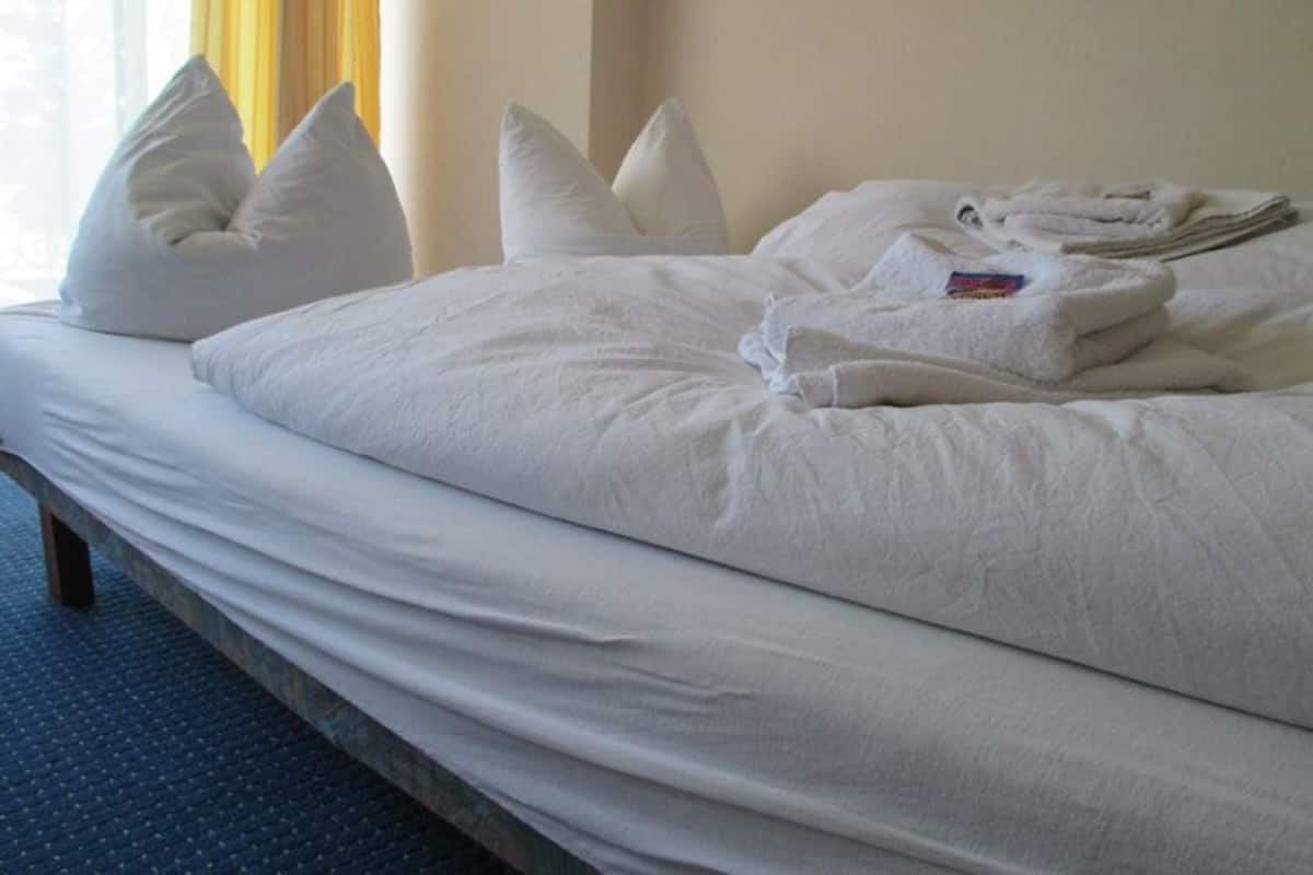 Una cama bien hecha con almohadas y toallas dobladas, un cabecero de madera y una ventana con cortinas.