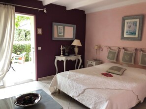 A bedroom with a large bed, a nightstand, a table with a lamp, and a window with curtains.