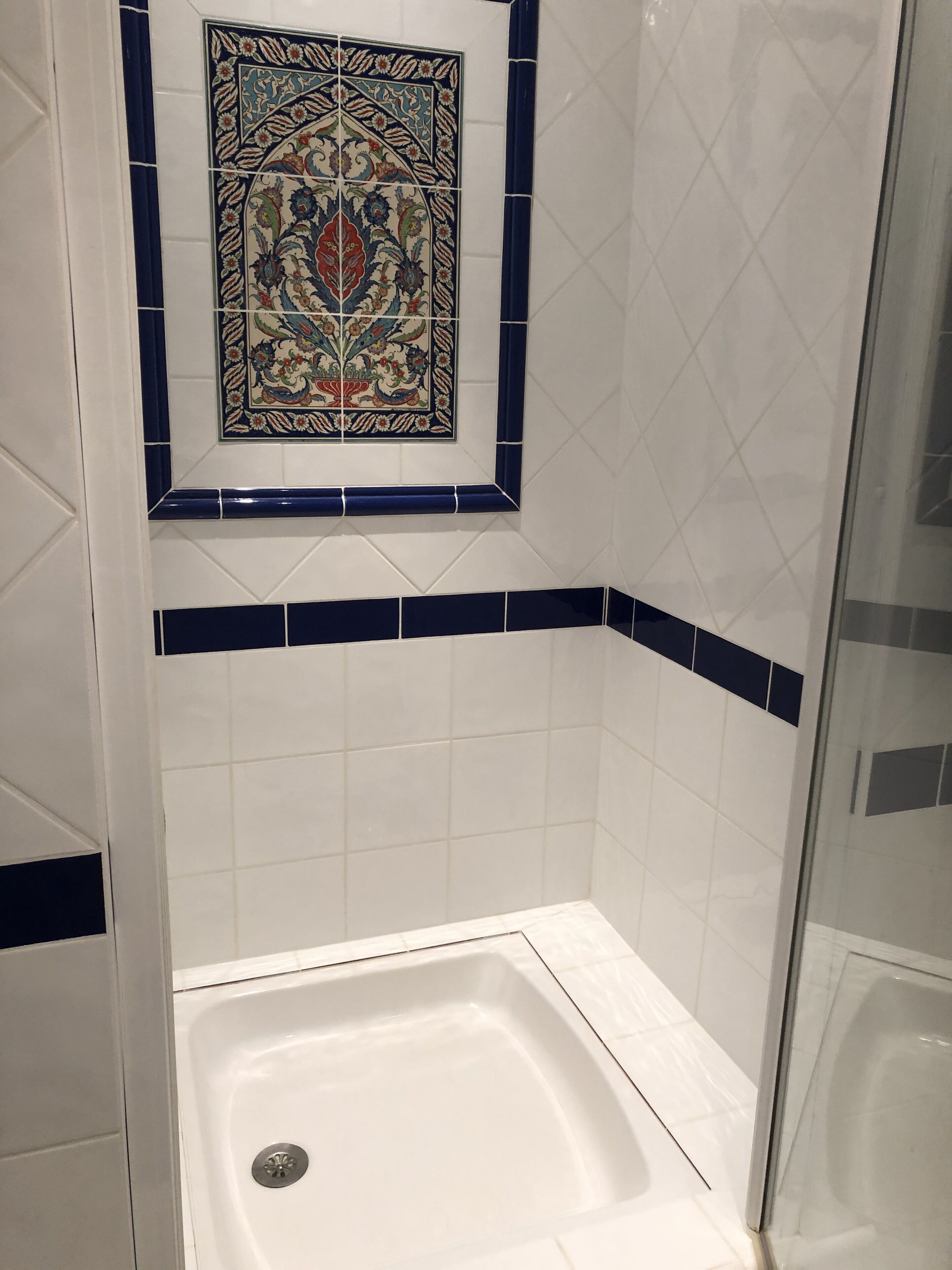A bathroom with a shower area, white tiles, and a decorative tile with floral patterns above the shower.
