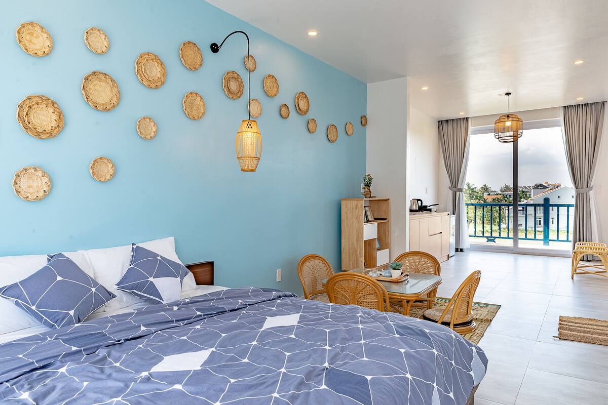 A bedroom with a large bed, a dining area with a table and chairs, and a balcony with a view.