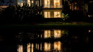 A multi-story building with balconies and a reflection in the water. - The Present Home Hoi An (Da Nang)