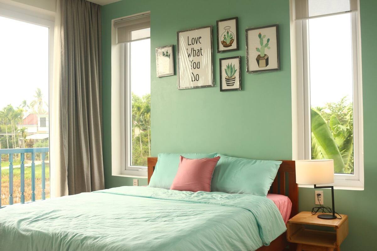 A bedroom with a bed, pillows, a nightstand with a lamp, and framed pictures on the wall.