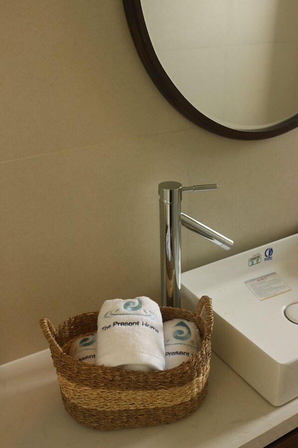 Un baño con un lavabo blanco, un grifo cromado y una cesta de mimbre con una toalla blanca que lleva un logo.