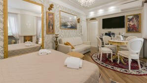 A hotel room with a large bed, a sitting area with a sofa and chairs, a dining table with chairs, a TV, and a chandelier.