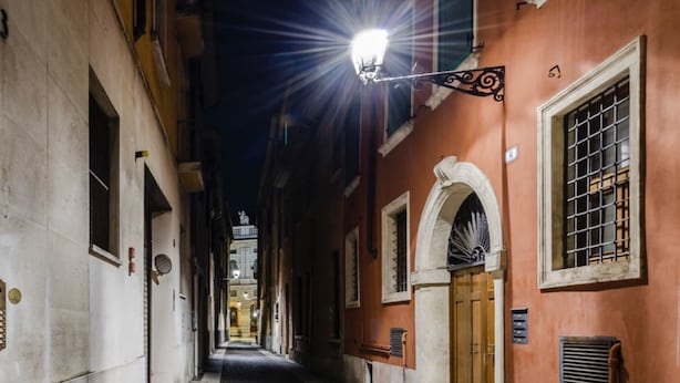 A narrow alleyway with buildings on either side, a street lamp, and a door with a metal gate.