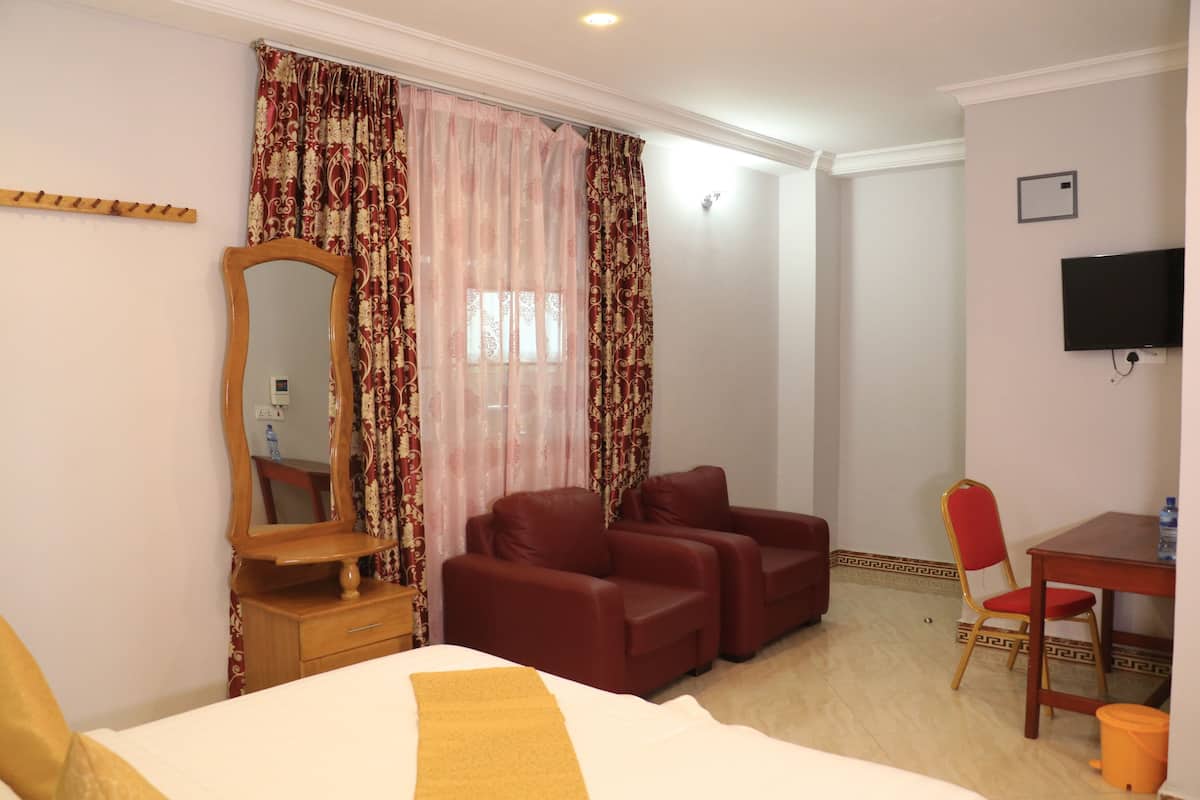 A hotel room with a bed, a wooden dresser, a mirror, a TV, a red sofa, a red chair, and a small table.