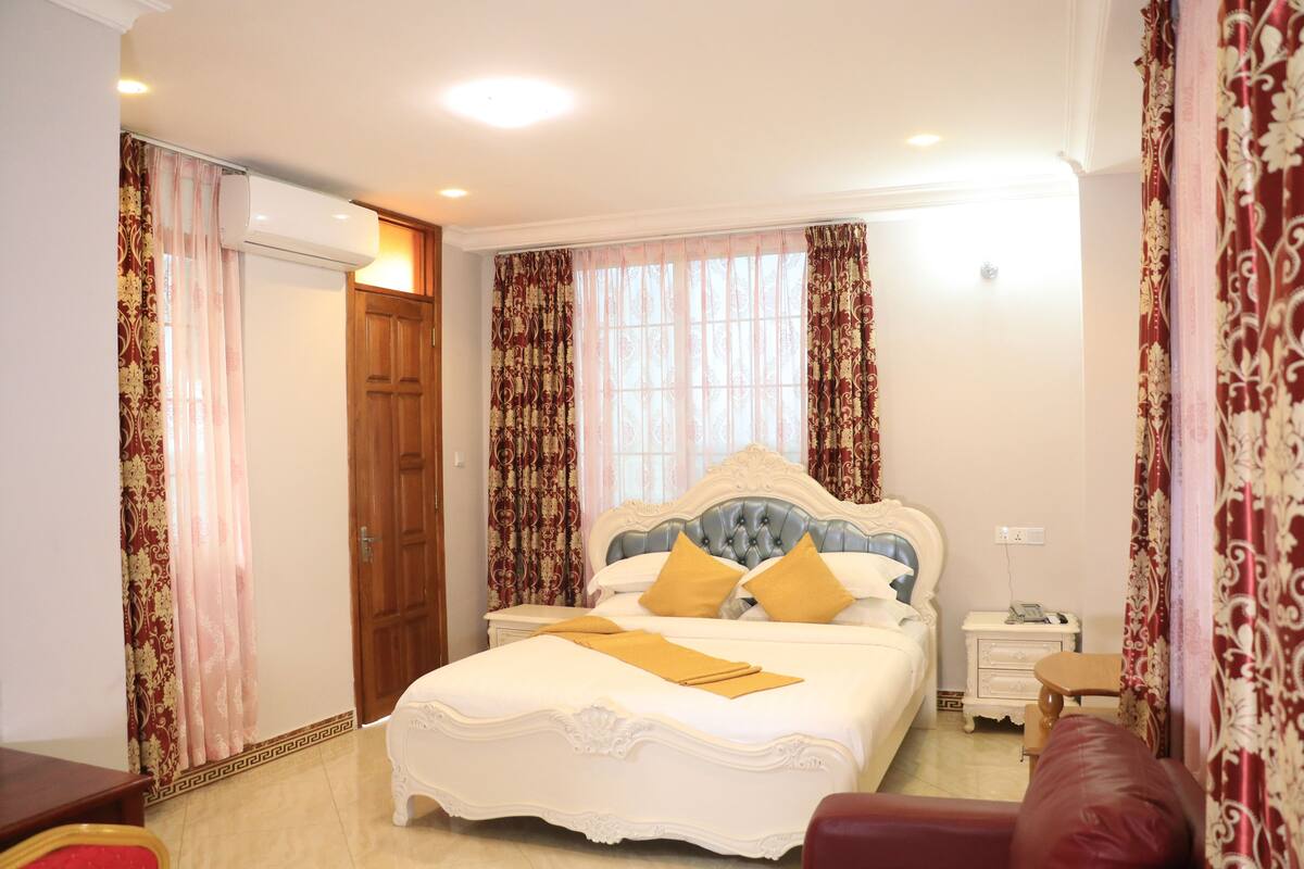 A bedroom with a large bed, a wooden door, a bedside table, and a red chair.