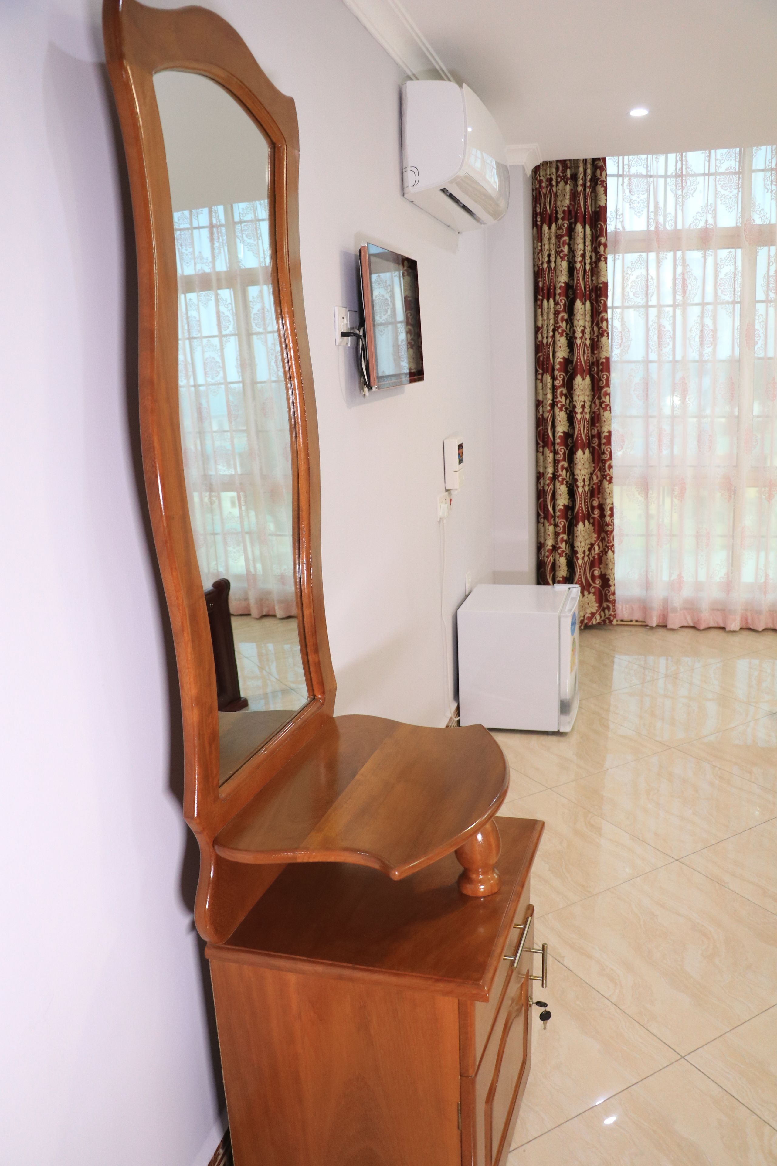 A room with a wooden vanity, a large mirror, a television, and a window with patterned curtains.