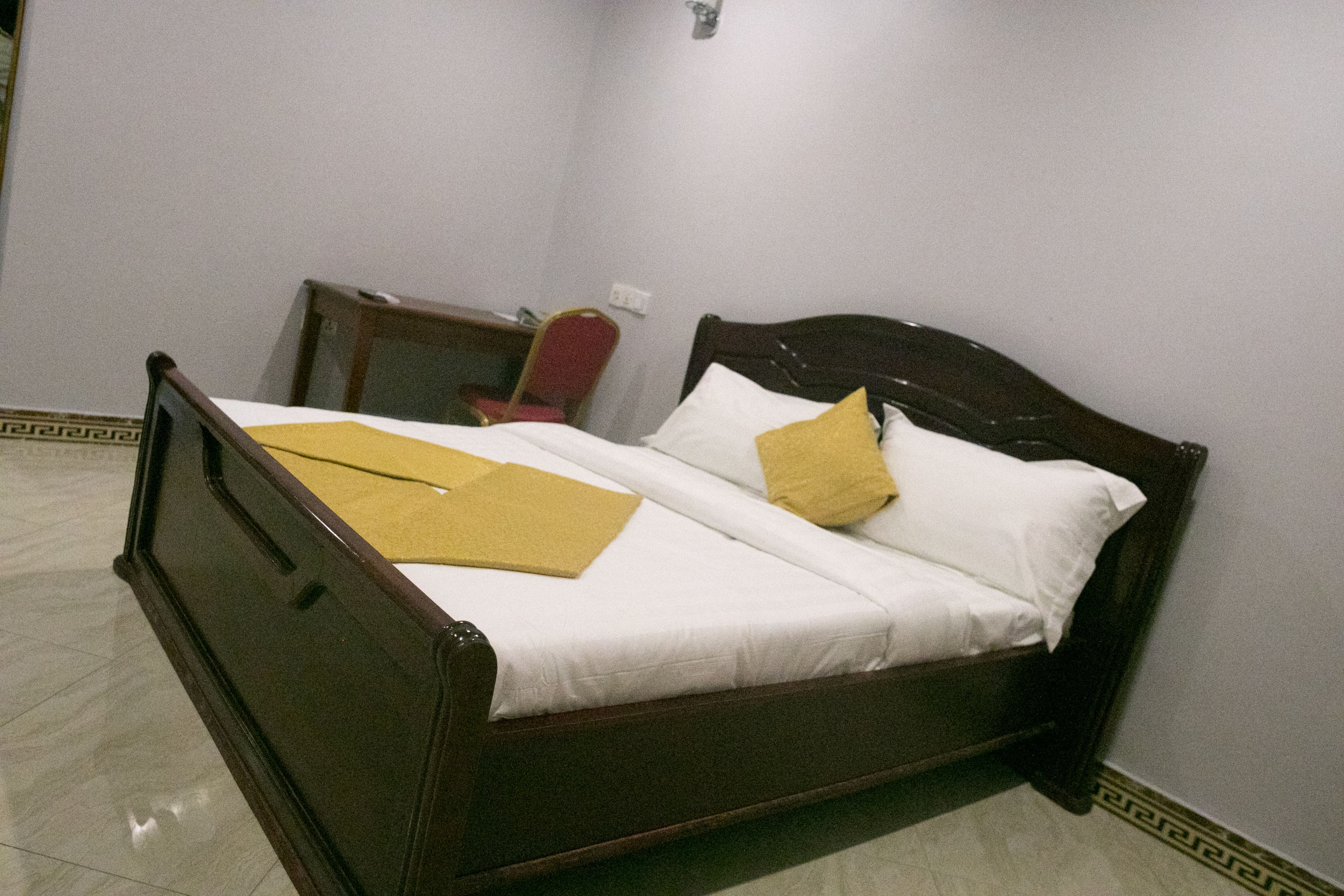 A single bed with a wooden frame, white bedding, and two yellow pillows.