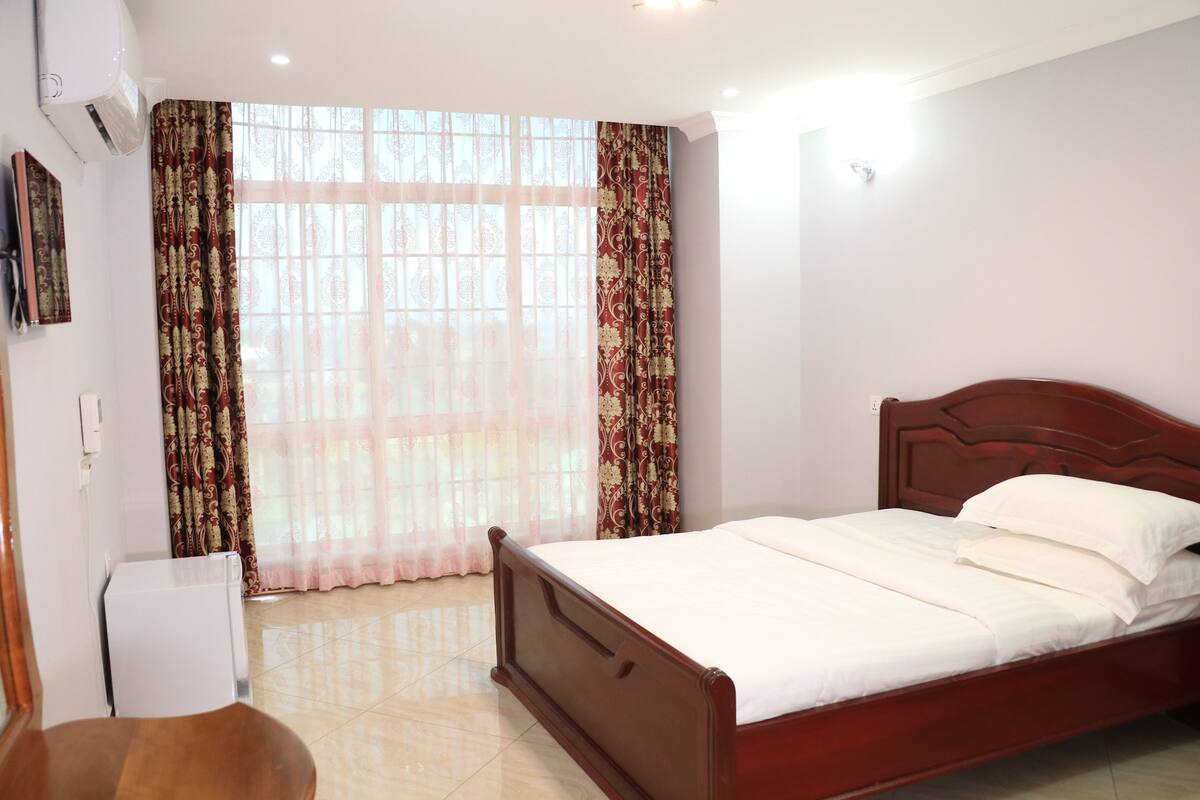 A bedroom with a wooden bed, a chair, a small table, and a window with curtains.