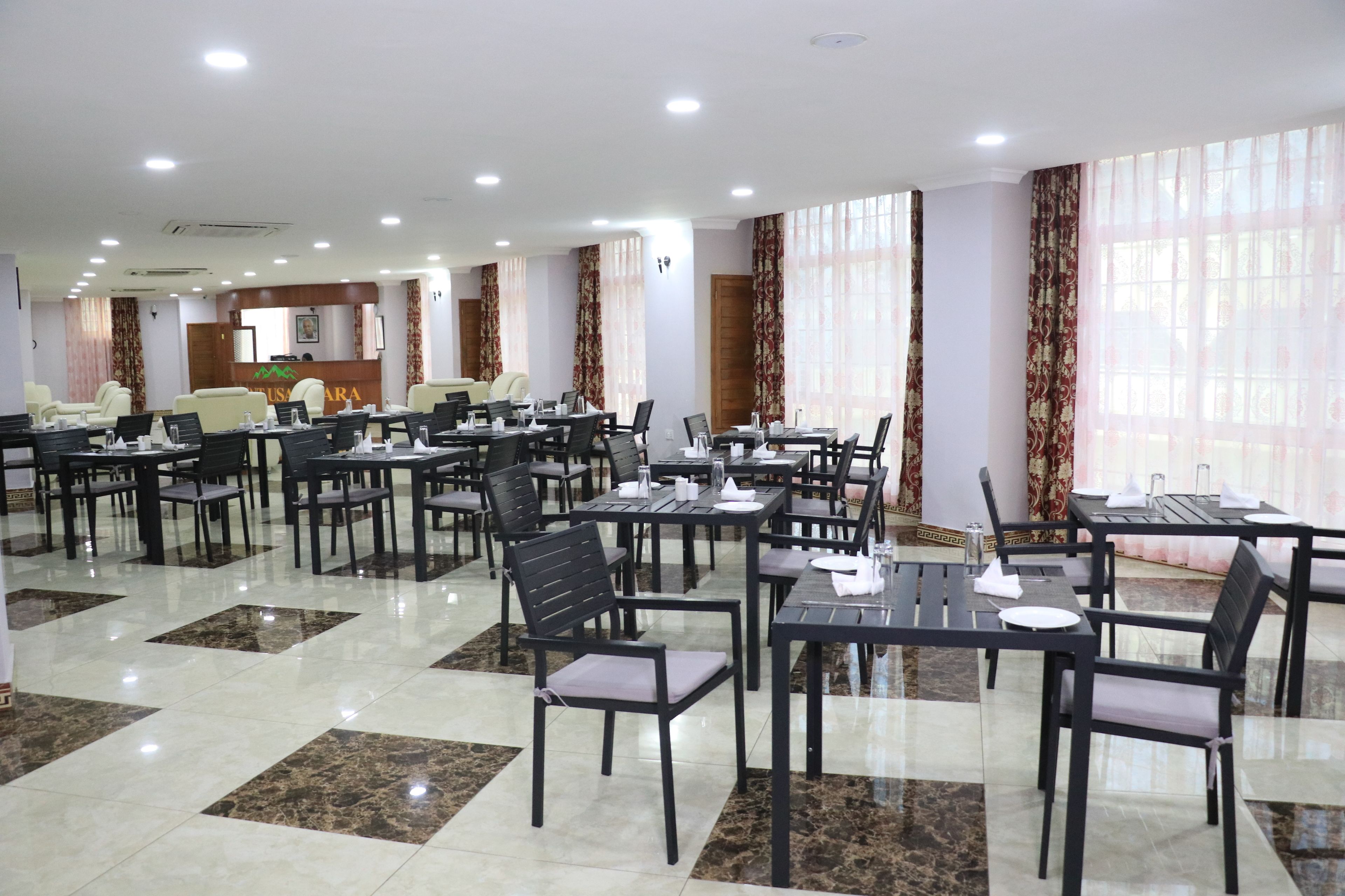 A spacious dining area with multiple tables and chairs, a reception desk, and large windows with curtains.