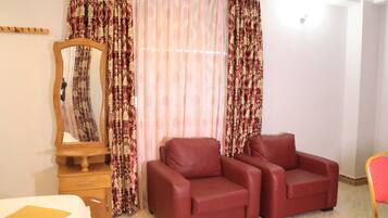 Una habitación con una cama, un aparador de madera, un espejo, dos sillones de cuero rojo y cortinas estampadas.