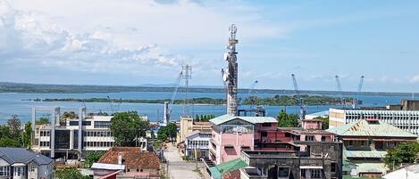 A coastal town with a prominent communication tower, buildings with varied architecture, and a view of the sea and distant islands.