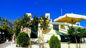 Un edificio moderno con fachada amarilla, un paraguas grande y una estatua en primer plano.