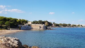 Zona costera con cielo despejado, costa rocosa y edificios a lo lejos.
