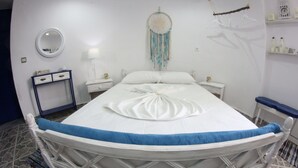 Una cama bien hecha con una toalla azul, una mesita de noche con lámpara, un aparador y un atrapasueños en la pared.