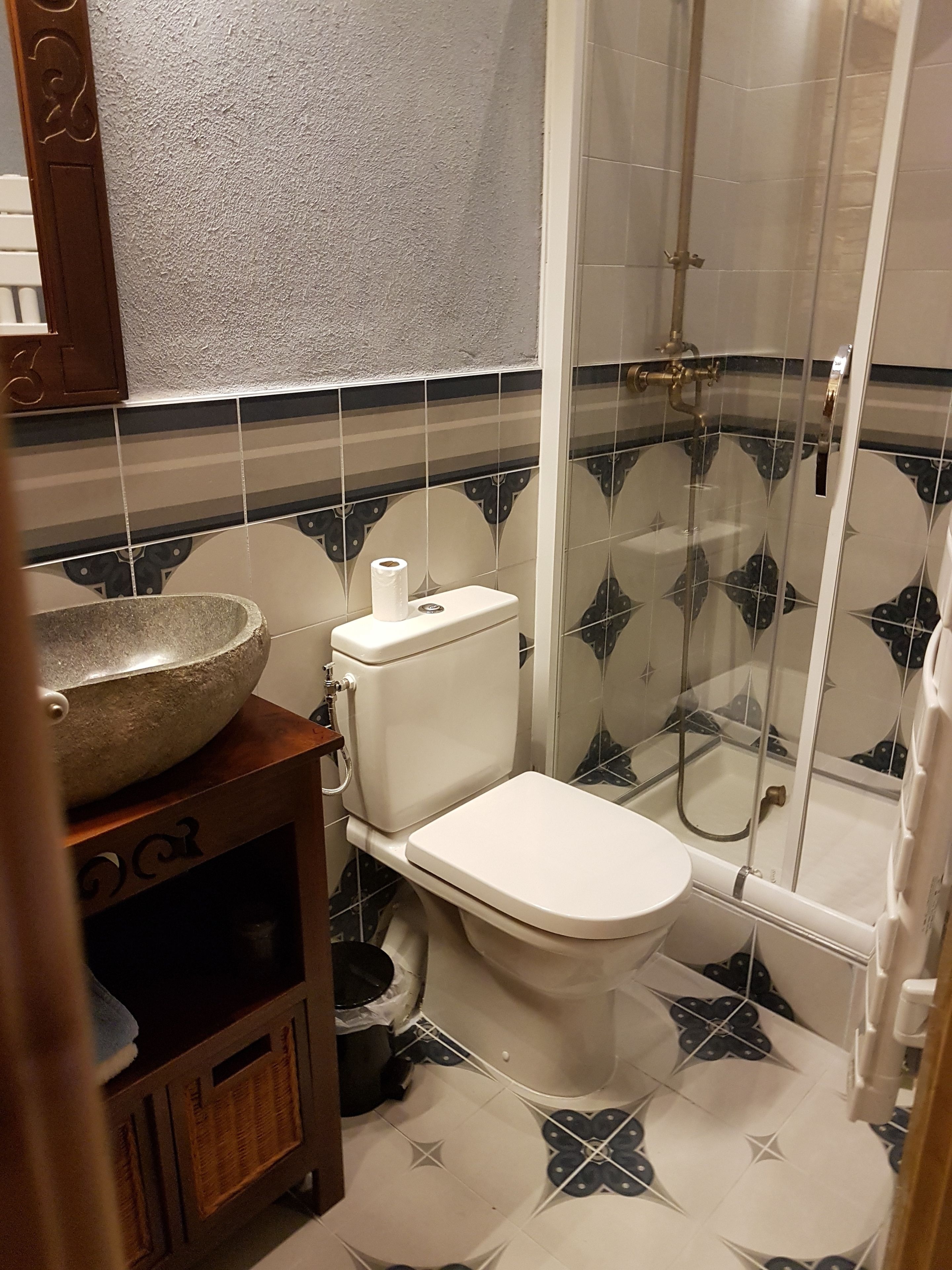 Une salle de bain comprenant des toilettes, un lavabo en pierre, une douche et des carreaux décorés.