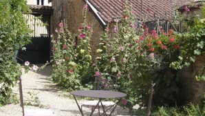 A garden with a table and chairs, a stone building, and a gate in the background. - La Maison des Gardes - Chambres d'hôtes (Cluny)