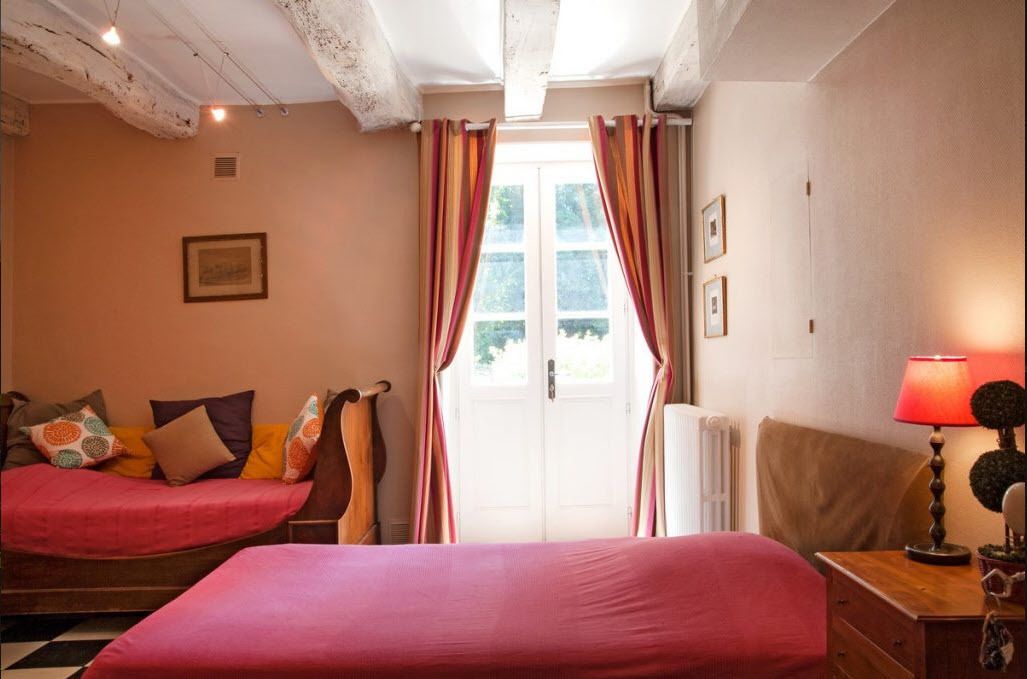 A bedroom with a bed, a sofa, a nightstand, and a window with curtains.