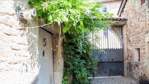 A narrow stone alley with a white wall, a metal door, and a gravel path. - La Maison des Gardes - Chambres d'hôtes (Cluny)