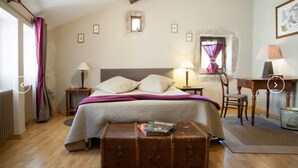 A bedroom with a bed, two bedside tables with lamps, a wooden chest, a desk with a chair, and a window with curtains. - La Maison des Gardes - Chambres d'hôtes (Cluny)