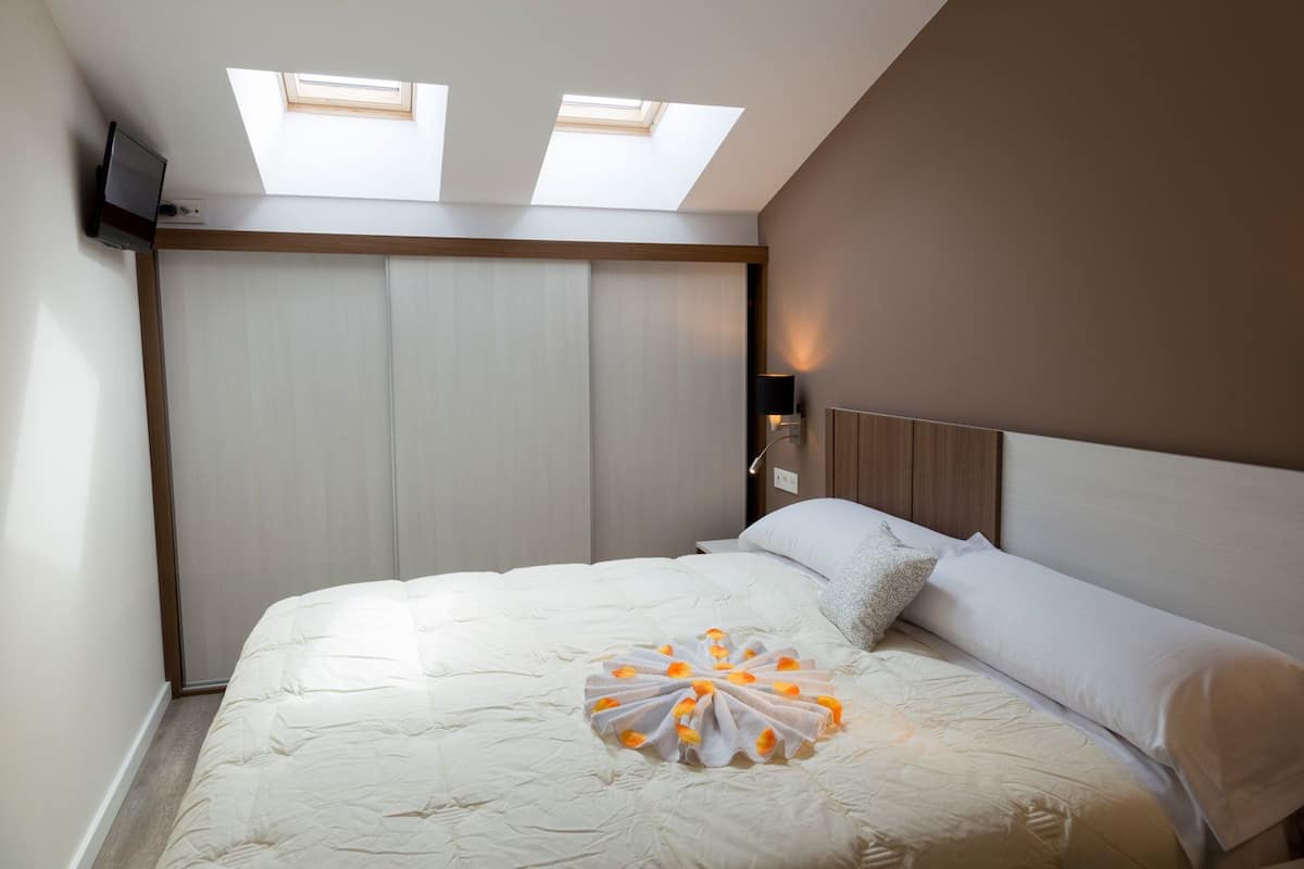Une chambre à coucher avec un lit, un téléviseur fixé au mur et des fenêtres de toit.