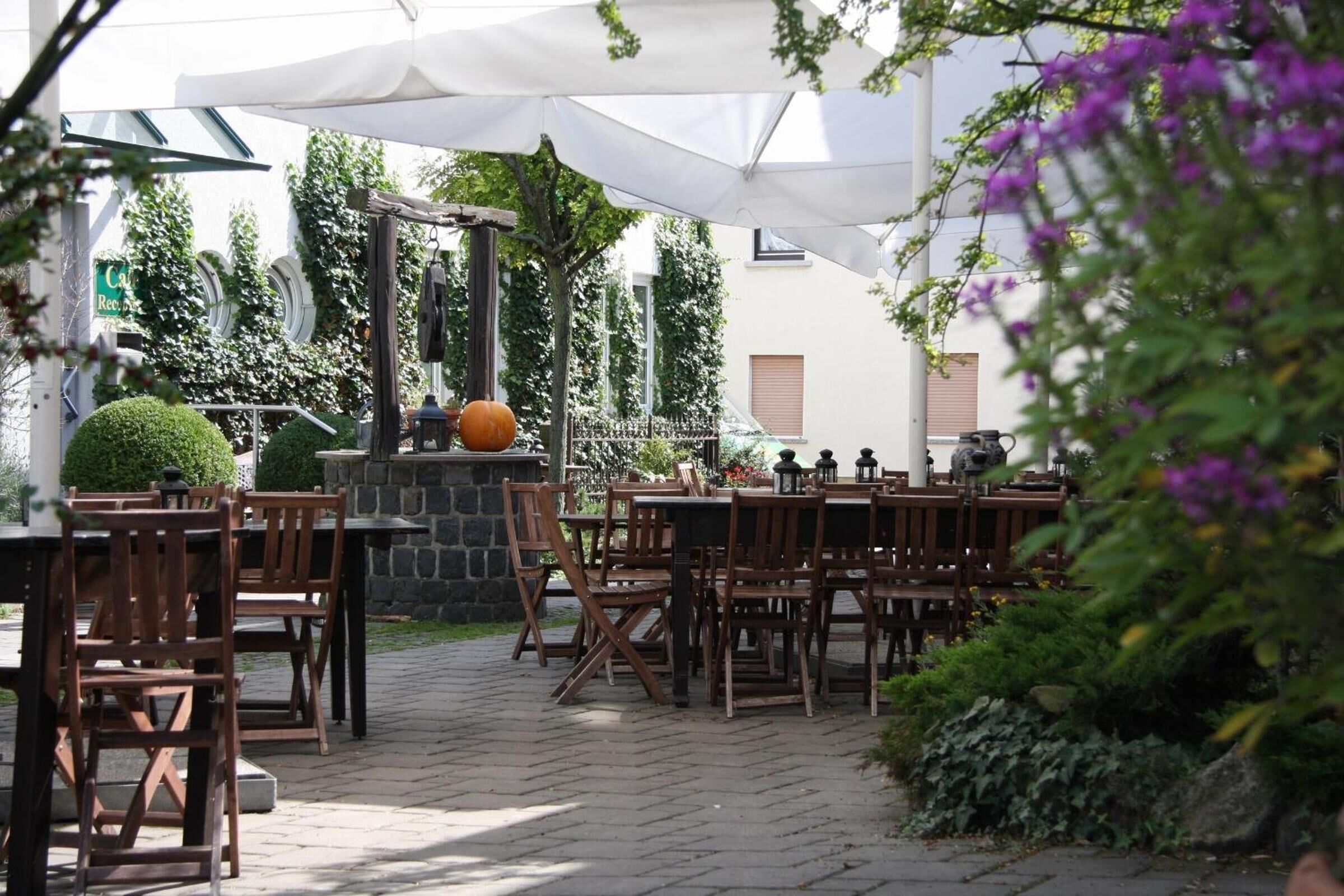 An outdoor patio with wooden tables and chairs, stone flooring, and a stone fireplace.