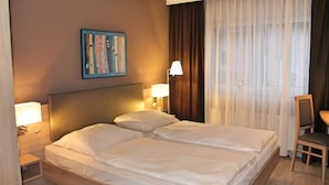 A hotel room with a double bed, two bedside lamps, a desk with a chair, a painting on the wall, and a window with curtains. - Hotel Gasthof Gruener Wald (Hofheim am Taunus)