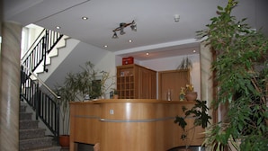A reception desk with a curved design, a staircase with black railings, and several potted plants. - Hotel Gasthof Gruener Wald (Hofheim am Taunus)