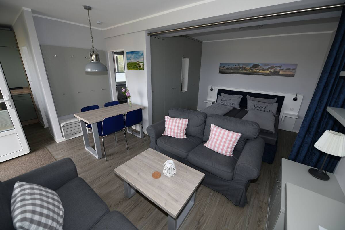 A modern living room with a grey sofa, a wooden coffee table, and a dining area with blue chairs.