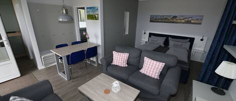 Una sala de estar moderna con un sofá gris, una mesa de centro de madera y un comedor con sillas azules.