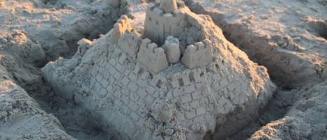 Un castillo de arena con una torre central y murallas circundantes, rodeado de arena.