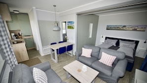 A modern living room with a grey sofa, a coffee table, and a dining area with a table and chairs. - Landhaus Dircks (St. Peter-Ording)