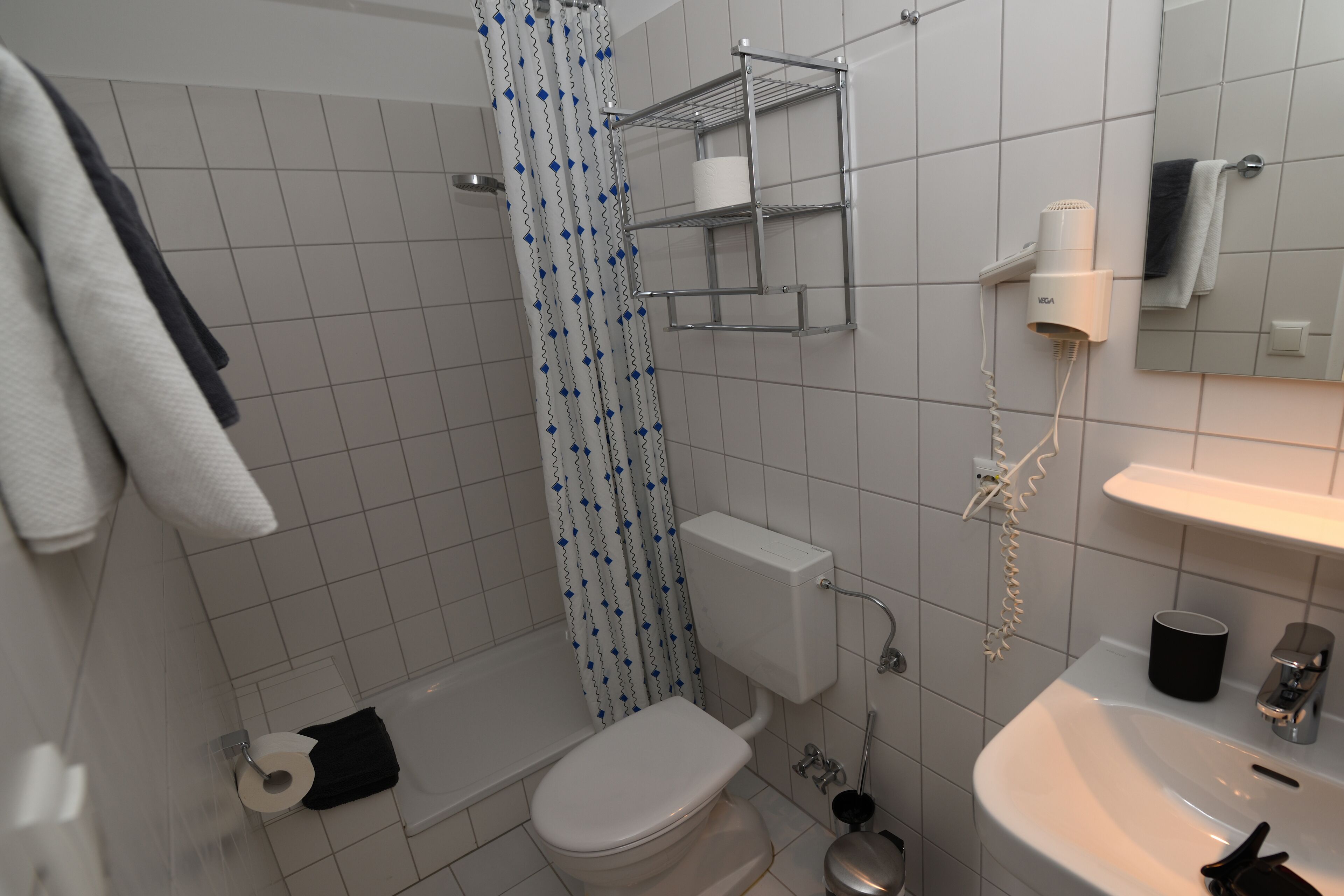 A bathroom with a toilet, shower, sink, and a towel rack.