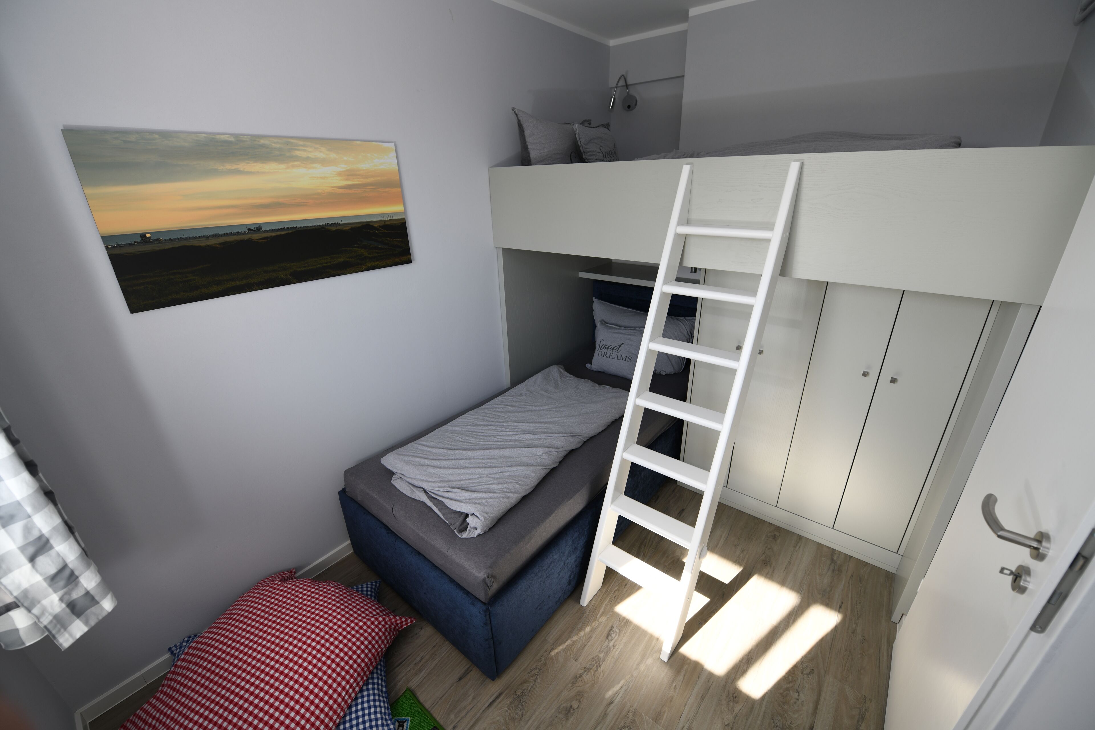 Un dormitorio compacto con una cama litera, una escalera, una mesita de noche pequeña y una cama individual.
