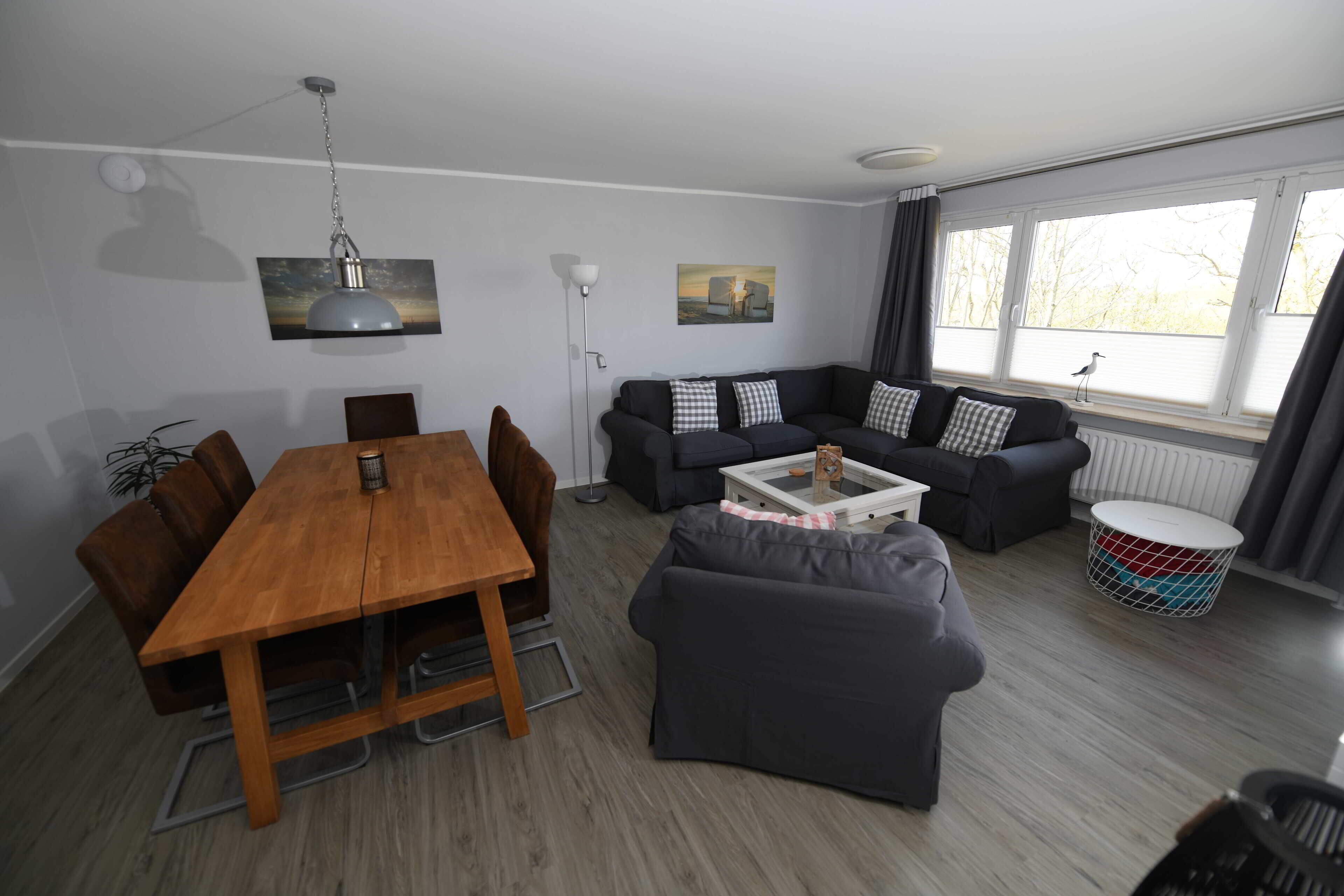 A modern living room with a wooden dining table, two sofas, a coffee table, and a large window with curtains.