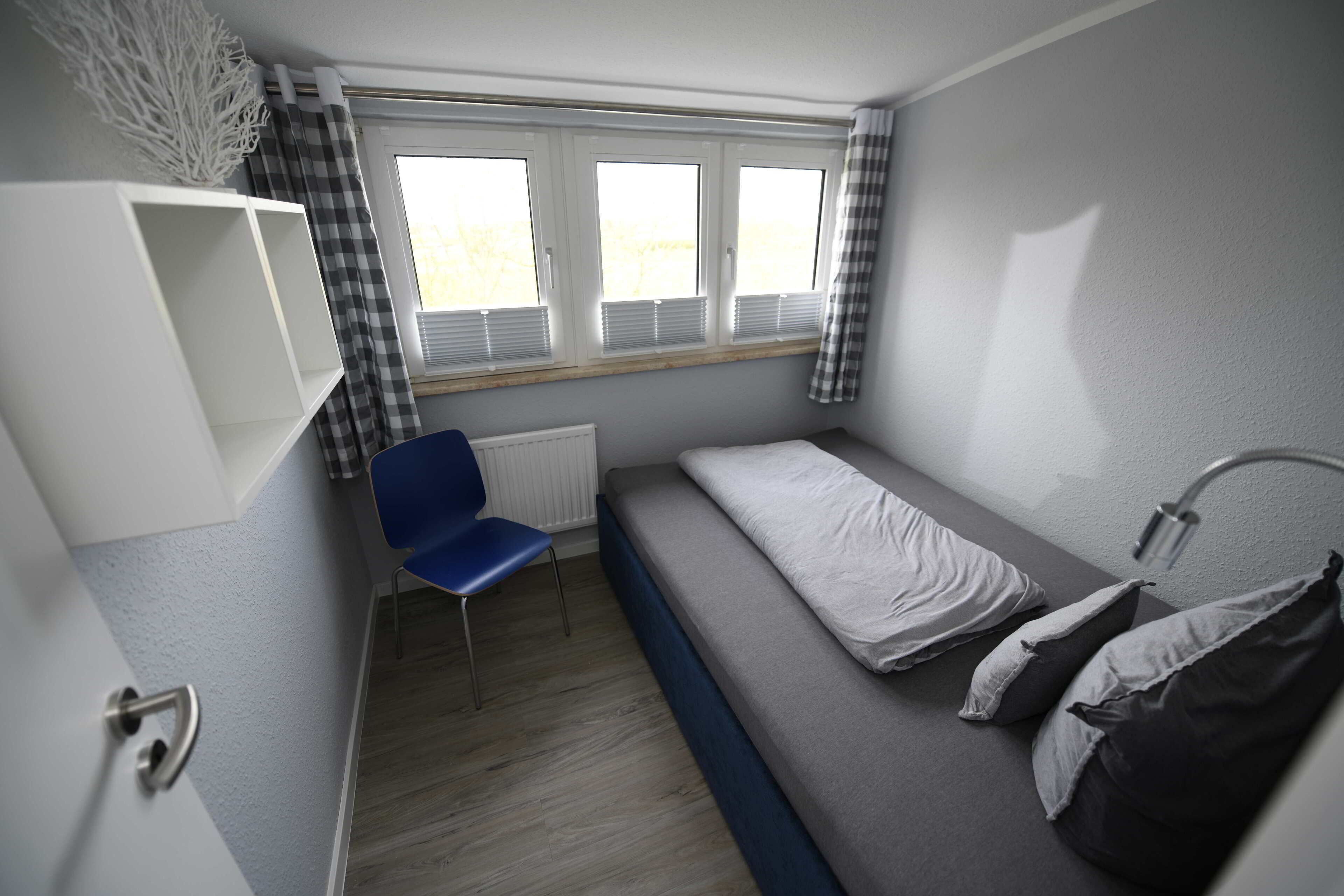 Una habitación pequeña con cama individual, ventana, silla y radiador.