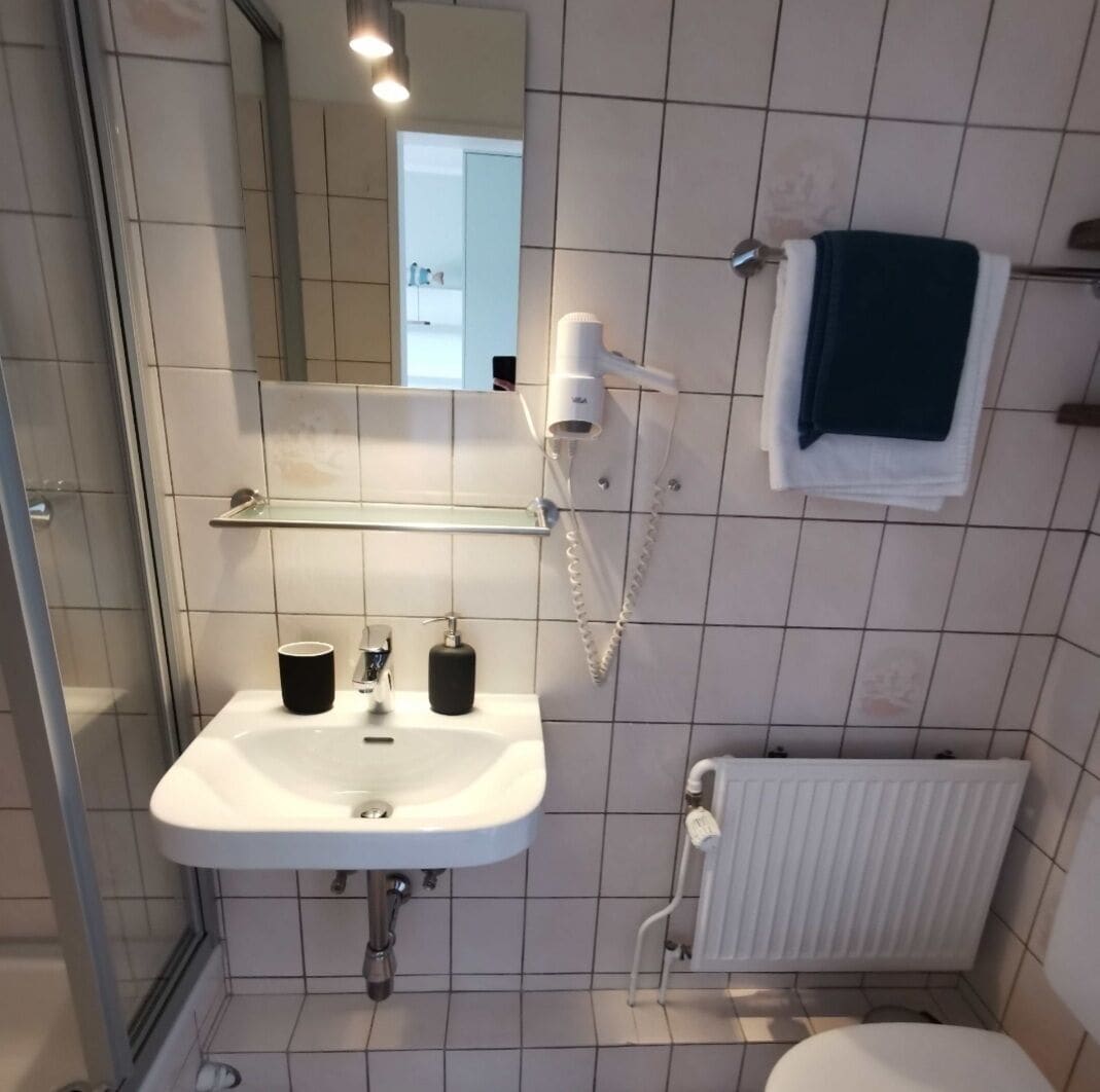 Une salle de bain avec un lavabo blanc, un miroir, un porte-serviettes et un espace douche.