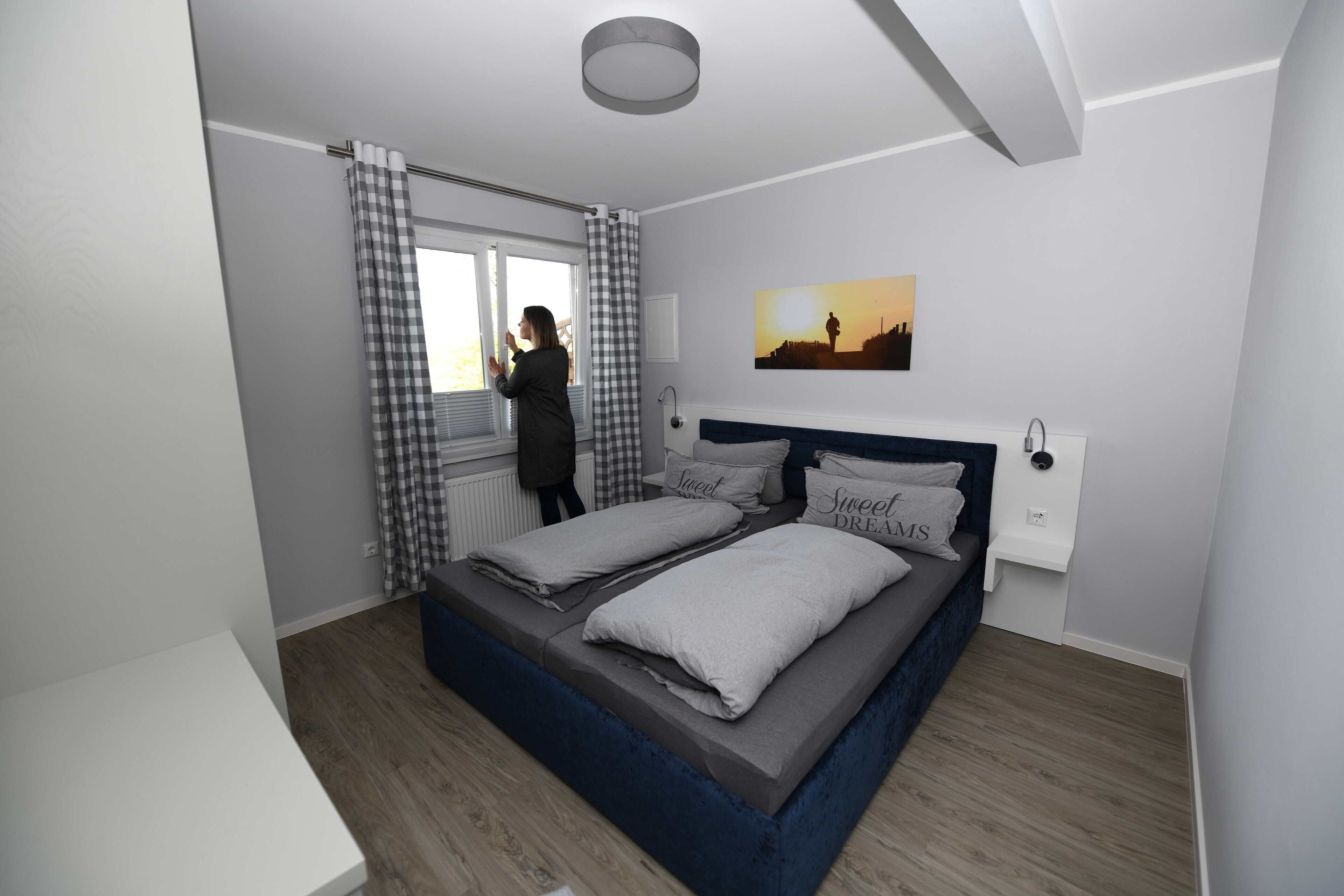 A bedroom with a bed, a window with curtains, a painting on the wall, and a bedside table.