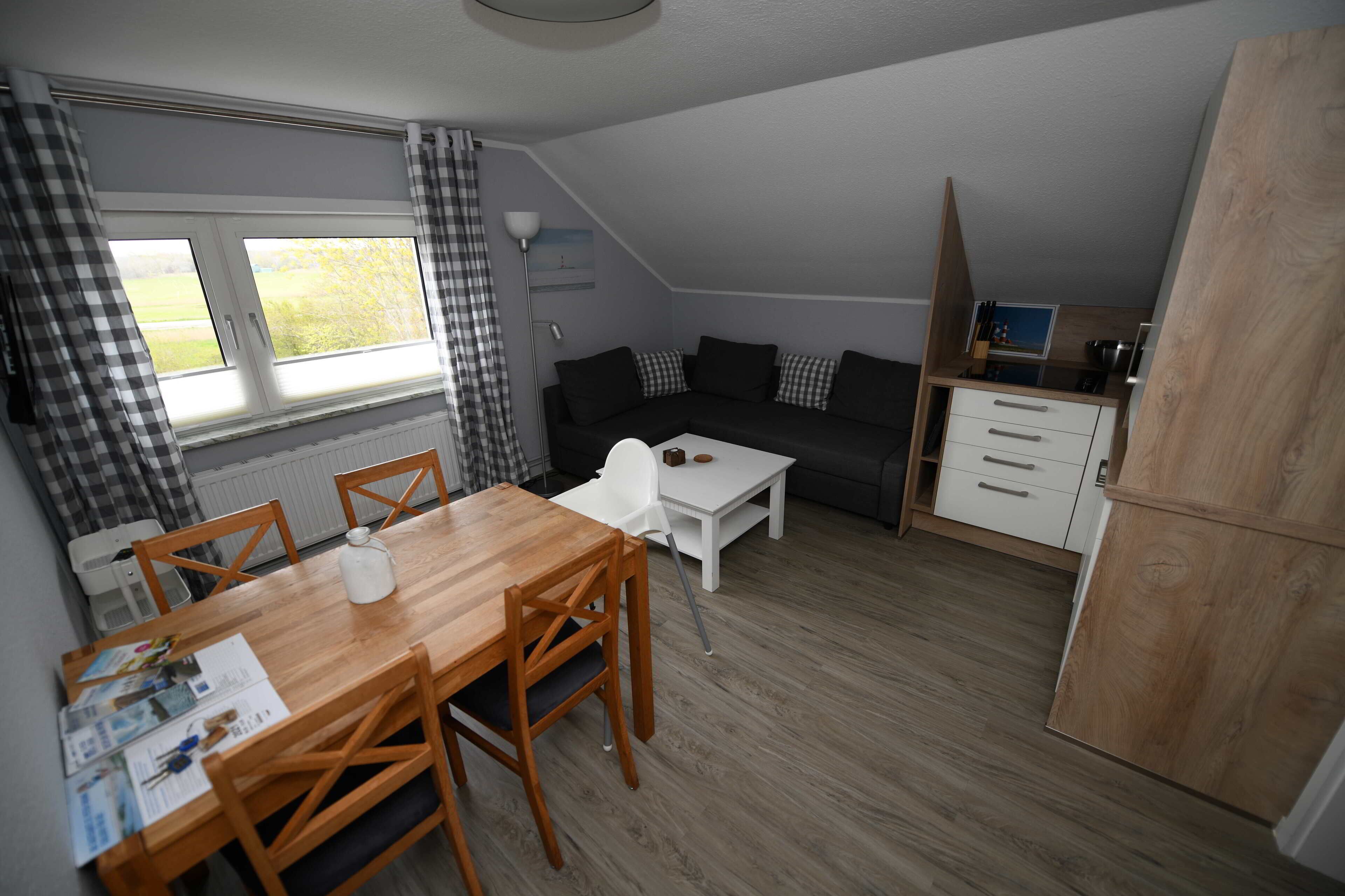 A compact living space with a dining area, a sofa, a small kitchen, and a window with curtains.