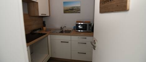 A compact kitchen with white cabinets, a wooden countertop, a microwave, and a sink.
