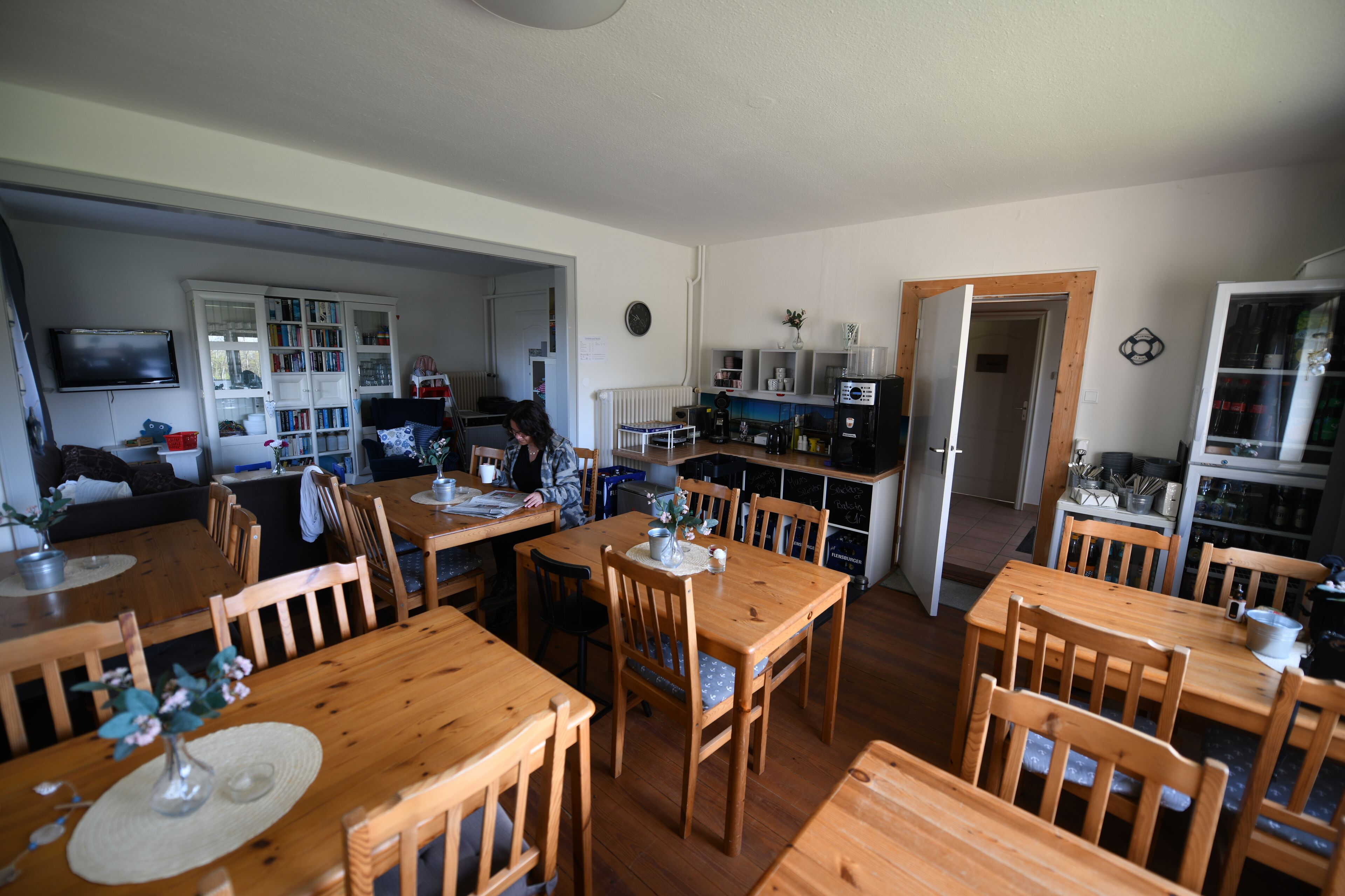 Een eethoek met houten tafels en stoelen, een keuken op de achtergrond en een televisie aan de muur.