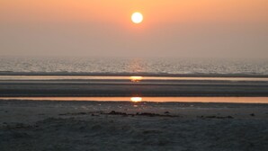 A beach scene with the sun setting over the horizon, reflecting on the water. - Landhaus Dircks (St. Peter-Ording)