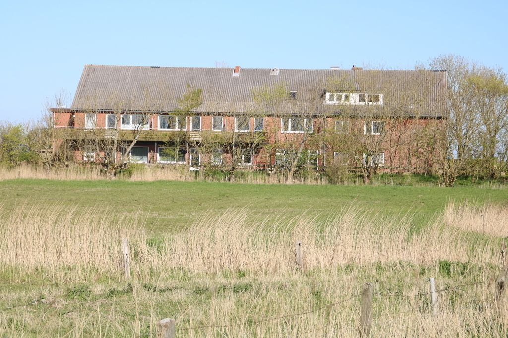 Ein zweistöckiges Backsteingebäude mit flachem Dach, umgeben von einer Wiese und einem Zaun.