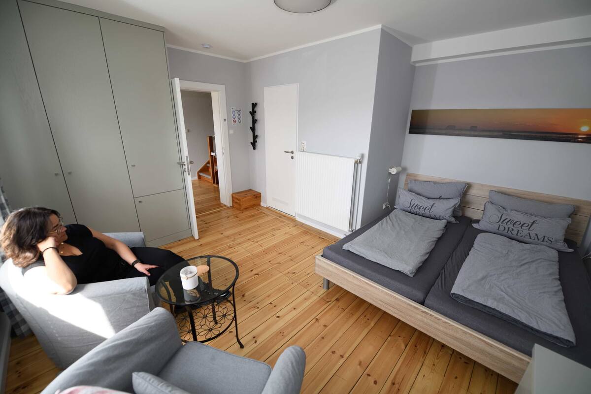 A bedroom with a bed, a grey sofa, a small table with a cup, and a wardrobe.